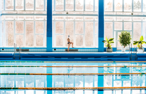 Senior man standing by the indoor swimming pool. Active pensioner enjoying sport.