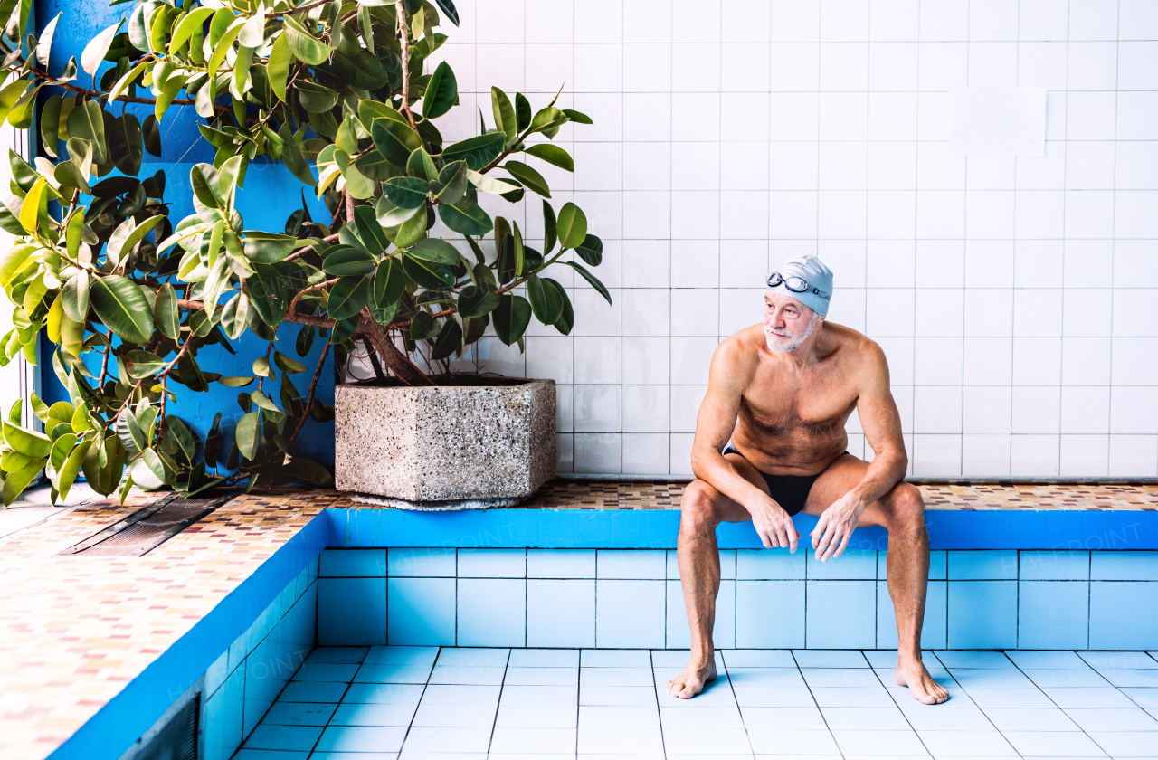 Senior man sitting by the indoor swimming pool. Active pensioner enjoying sport.