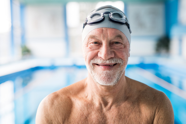 Senior man standing in an indoor swimming pool. Active pensioner enjoying sport.