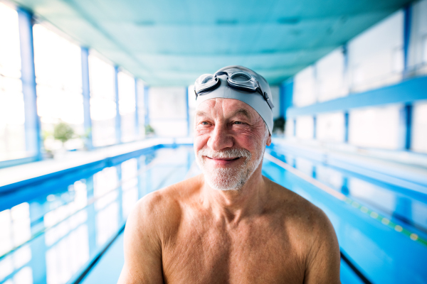 Senior man standing in an indoor swimming pool. Active pensioner enjoying sport.