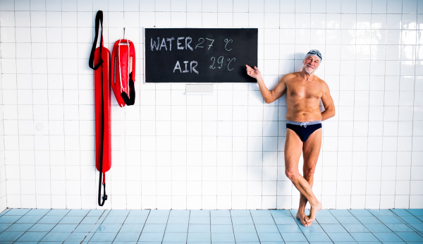 Senior man standing in an indoor swimming pool. Active pensioner enjoying sport.