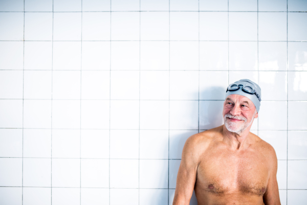 Portrait of a senior man standing against white background in an indoor swimming pool. Active pensioner enjoying sport.