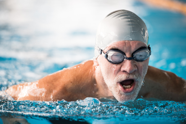 Senior man swimming in an indoor swimming pool. Active pensioner enjoying sport.