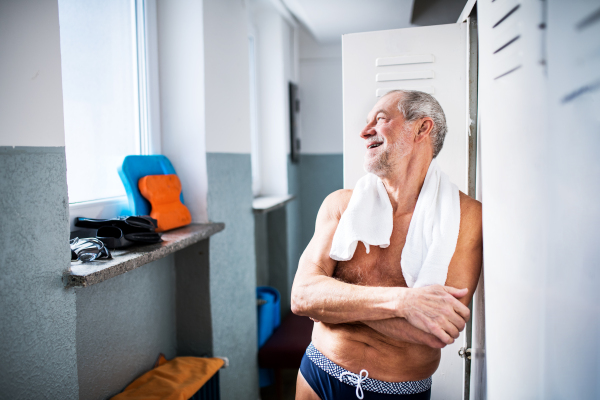 Senior man standing by the lockers in an indoor swimming pool. Active pensioner enjoying sport.