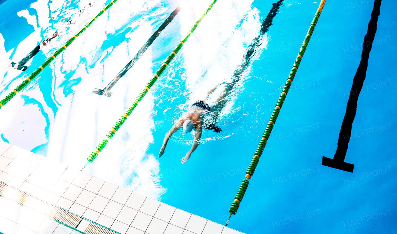 Senior man swimming in an indoor swimming pool. Active pensioner enjoying sport. Top view.