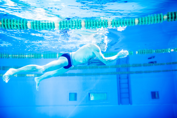 Senior man swimming underwater in an indoor swimming pool. Active pensioner enjoying sport.