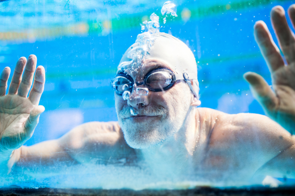 Senior man swimming underwater in an indoor swimming pool. Active pensioner enjoying sport. Close up.