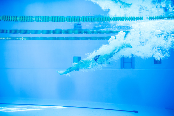 Senior man in an indoor swimming pool. Active pensioner enjoying sport. An old man jumping in the pool.