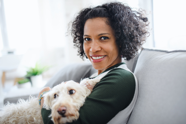 A portrait of happy mature woman with dog sitting indoors at home, looking at camera.