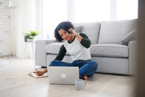 A portrait of happy mature woman working on laptop and making phone call indoors, home office concept.