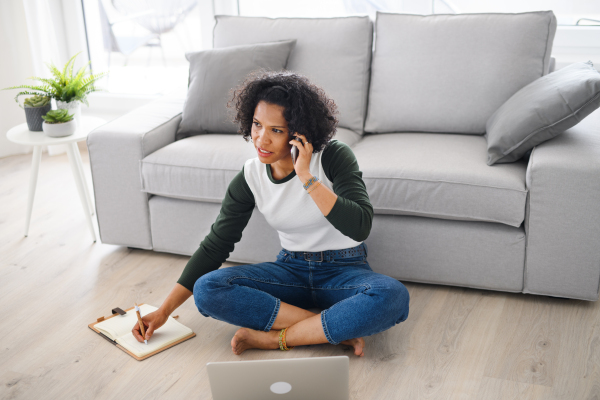 A portrait of happy mature woman working on laptop and making phone call indoors, home office concept.