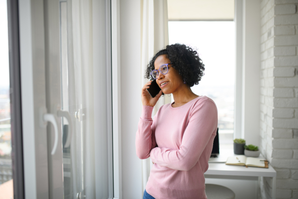 A portrait of happy mature woman making a phone call indoors, looking out of window.