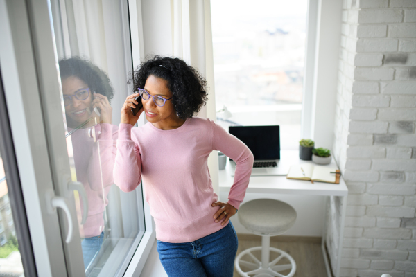 A portrait of happy mature woman making a phone call indoors, looking out of window.