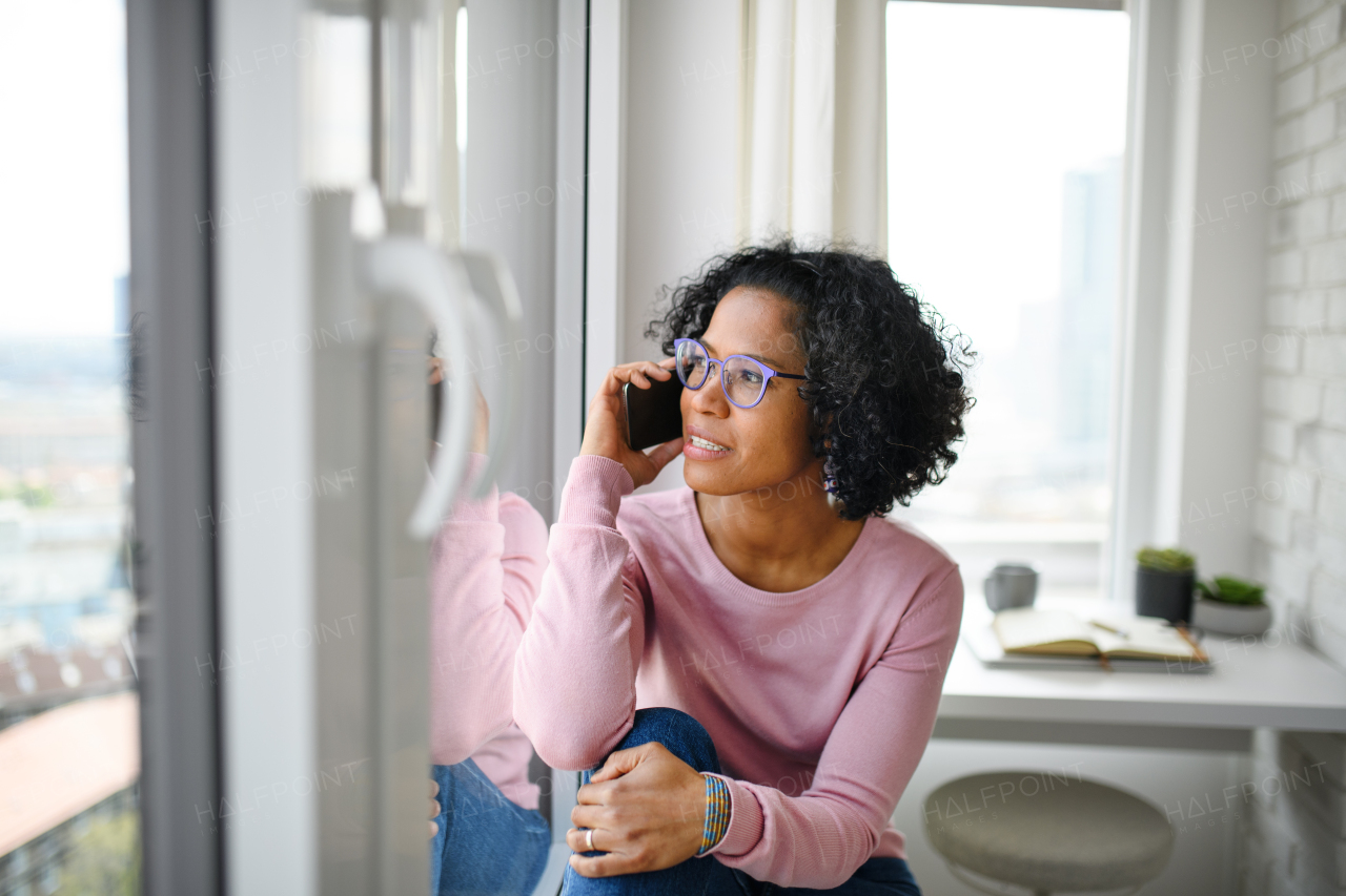 A portrait of happy mature woman making a phone call indoors, looking out of window.