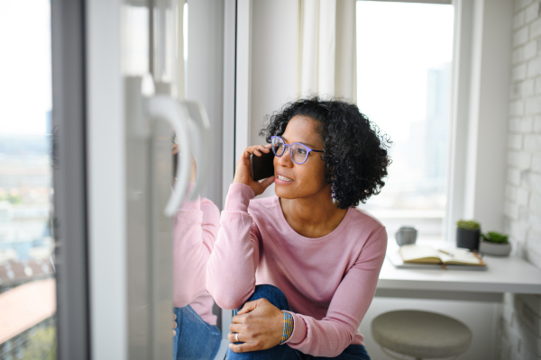 A portrait of happy mature woman making a phone call indoors, looking out of window.