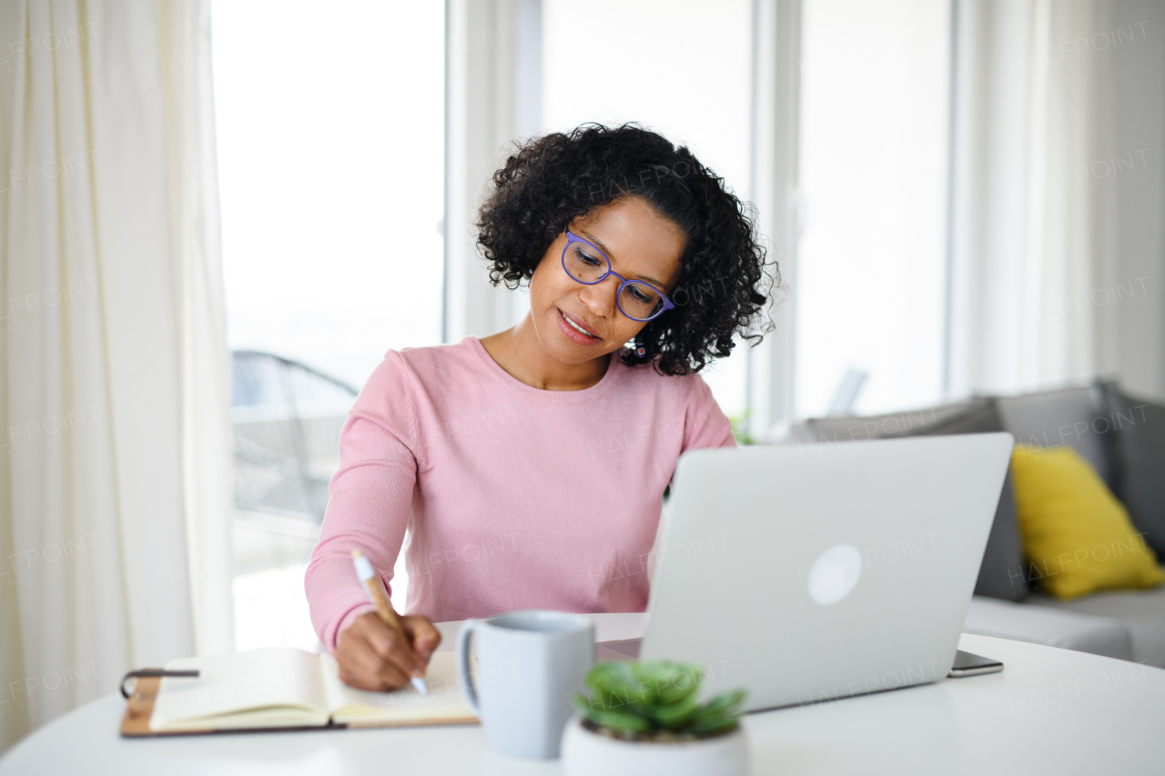 A portrait of happy mature woman working on laptop indoors, home office concept.