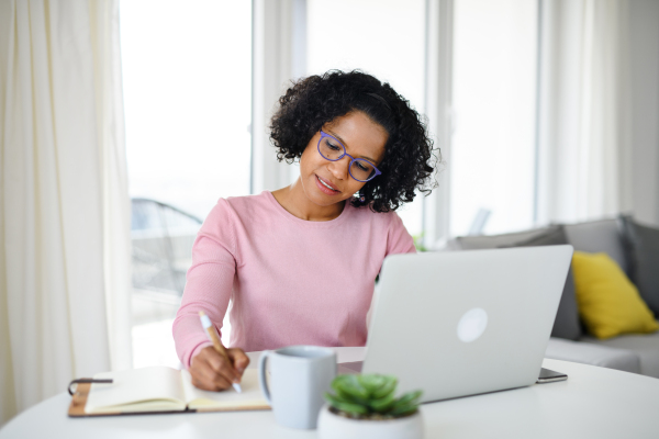 A portrait of happy mature woman working on laptop indoors, home office concept.