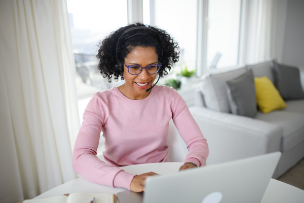 A portrait of happy mature woman with headset working on laptop indoors, home office concept.