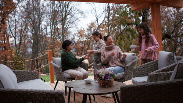 Two happy sisters with a mother and grandmother sitting and drinking tea outdoors in patio in autumn.