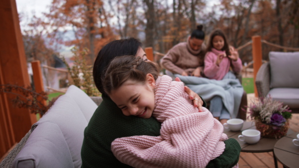 A happy little girl with grandmother sitting wrapped in blanket outdoors in patio in autumn