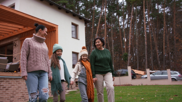 Two happy sisters with a mother and grandmother walking and holding hands outdoors in garden in autumn