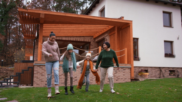 Two happy sisters with a mother and grandmother walking and holding hands outdoors in garden in autumn