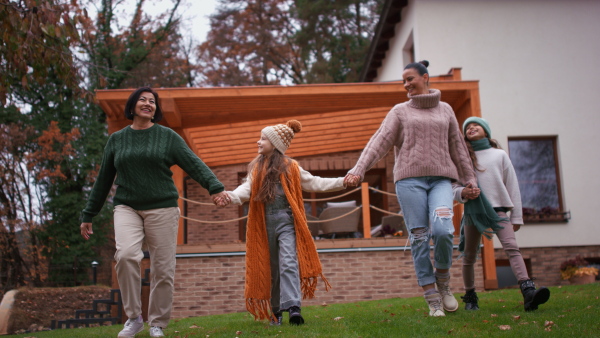 Two happy sisters with a mother and grandmother walking and holding hands outdoors in garden in autumn