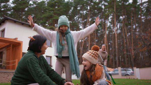 Happy little girls with a grandmother picking up leaves and putting them in bucket in garden in autumn