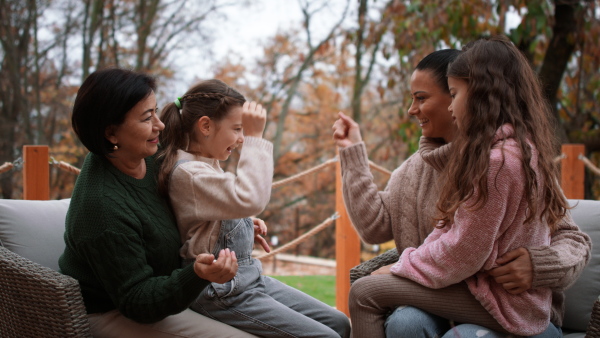 Two happy sisters with a mother and grandmother sitting and drinking tea outdoors in patio in autumn.