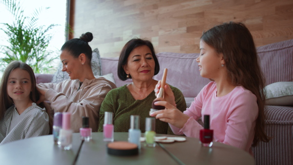 Two happy sisters with a mother and grandmother combing hair and doing make up together at home