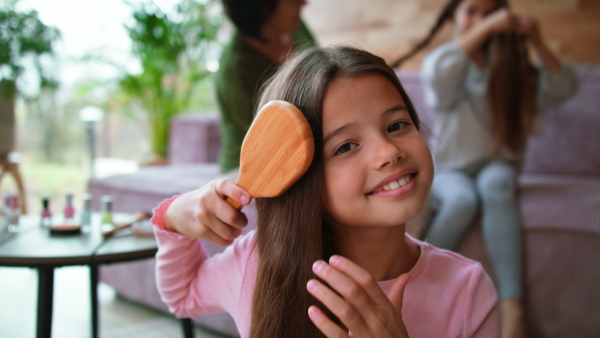 A happy little girl brushing her hair and looking at camera at home.