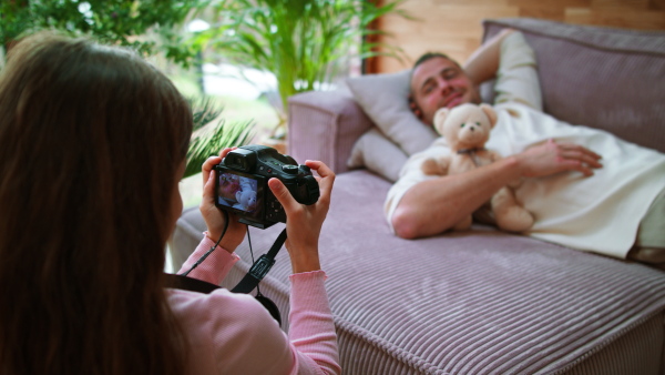 A little girl taking picture with camera of her father lying on sofa at home.