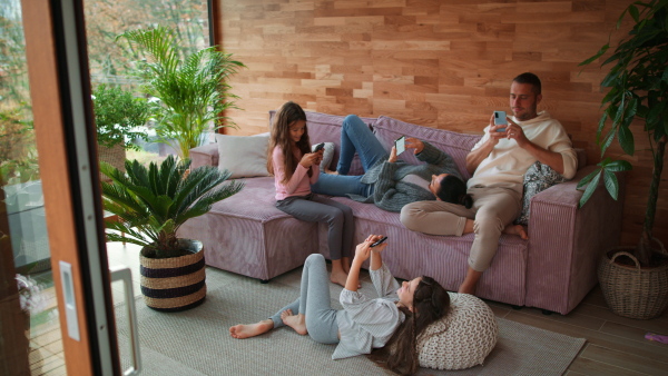 A family with two little daughters, everyone is using mobile phone in the living room.