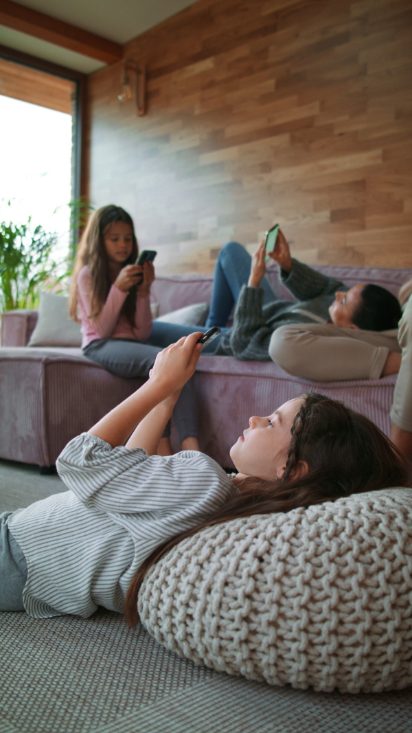 A vertical footage of mother with two little daughters, everyone is using mobile phone in the living room.