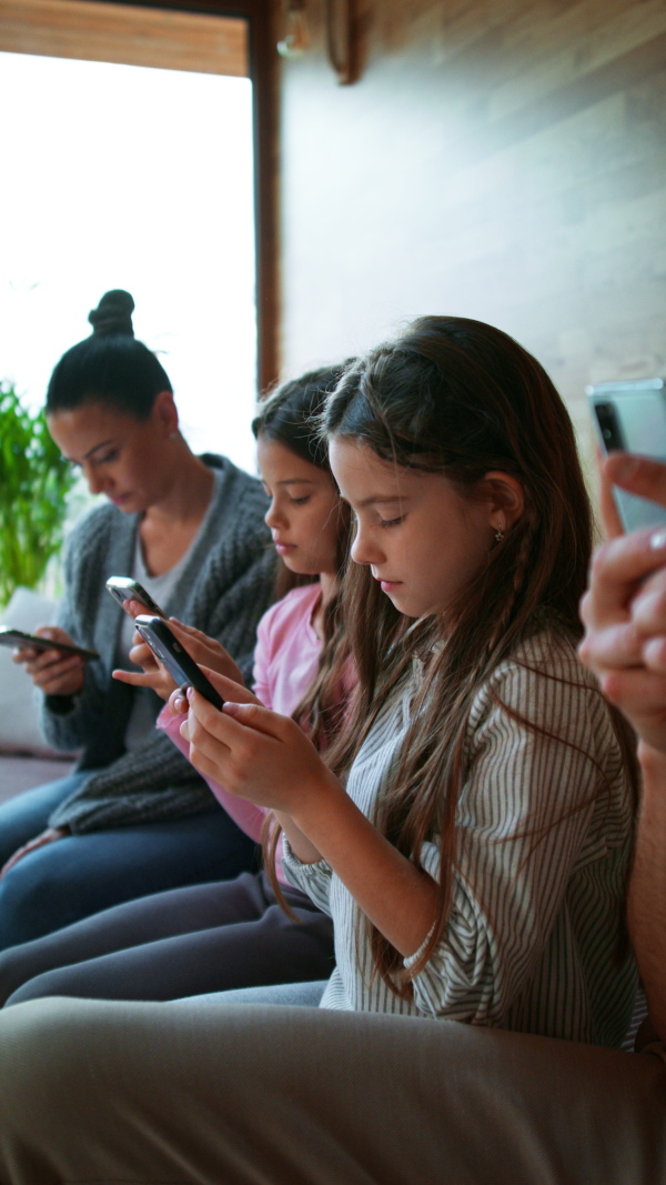 A vertical footage of family with two little daughters, everyone is using mobile phone in the living room.