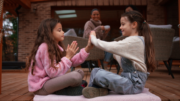 Two happy little sisters hugging outdoors in a patio in autumn, mother and grandmother at background.