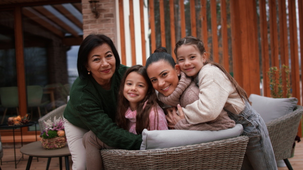 Two happy sisters with a mother and grandmother embracing and looking at camera outdoors in patio in autumn.