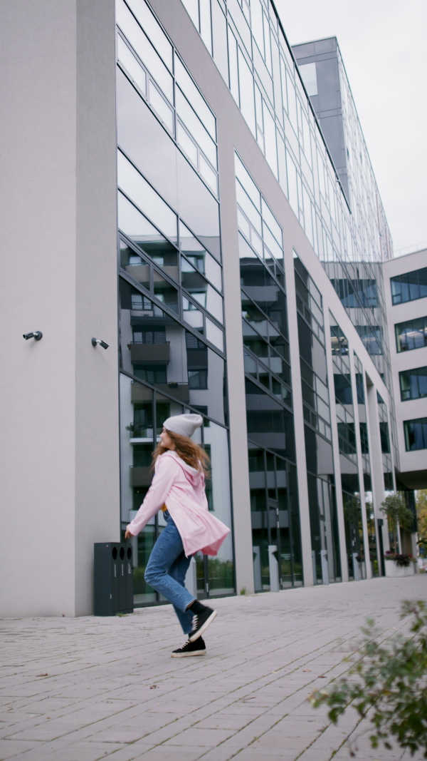 Young woman with hat dancing outdoors on street, vertical video.