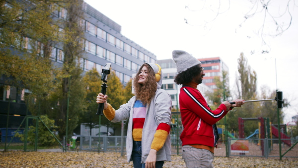 Portrait of young couple with smartphone making video for social media outdoors on street.