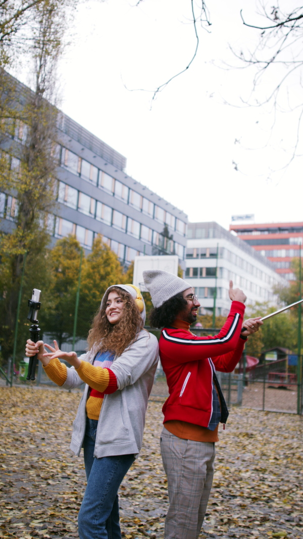 Portrait of young couple with smartphone making video for social media outdoors on street, vertical view.