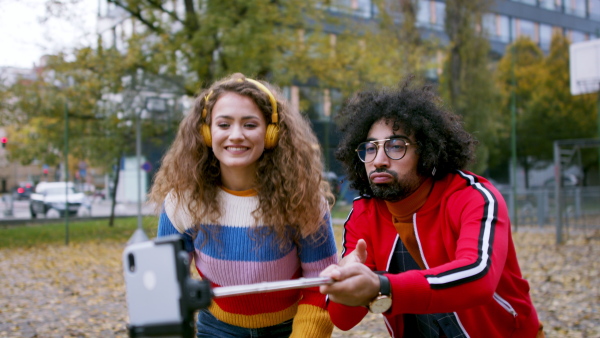 Portrait of young couple with smartphone making video for social media outdoors on street.