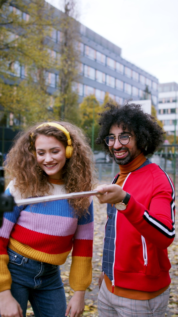 Portrait of young couple with smartphone making video for social media outdoors on street, vertical view.