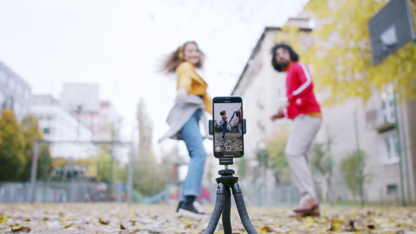 Portrait of young couple with smartphone making video for social media outdoors in park.