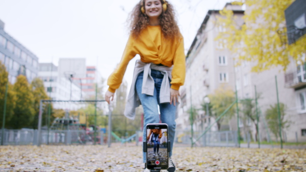 Young woman with smartphone making dance video for social media outdoors on street.