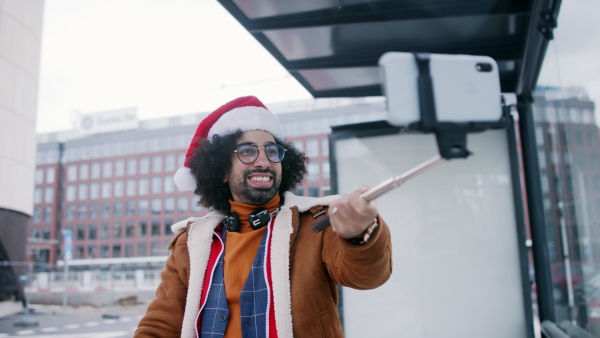 Young man with santa hat making video for social media outdoors on street.