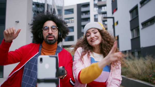 Young couple with smartphone making video for social media outdoors on street.