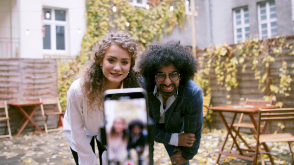 Portrait of young couple with smartphone making video for social media outdoors in park.