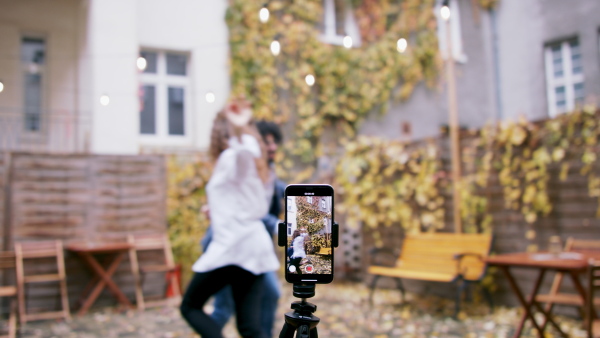 Portrait of young couple making dance video with smartphone outdoors on street, social media concept.