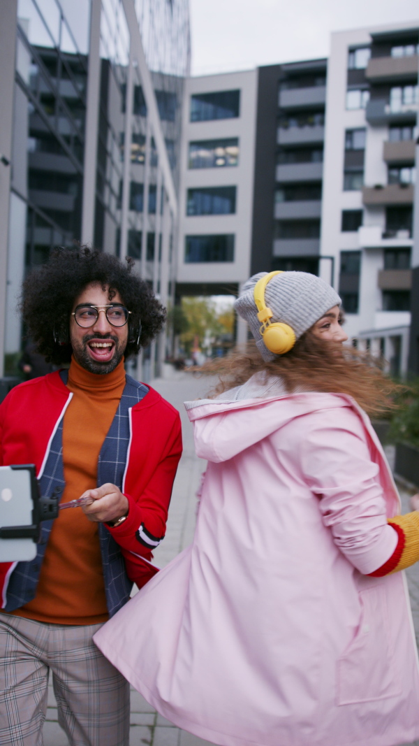 Young couple with smartphone making video for social media outdoors on street, vertical video.