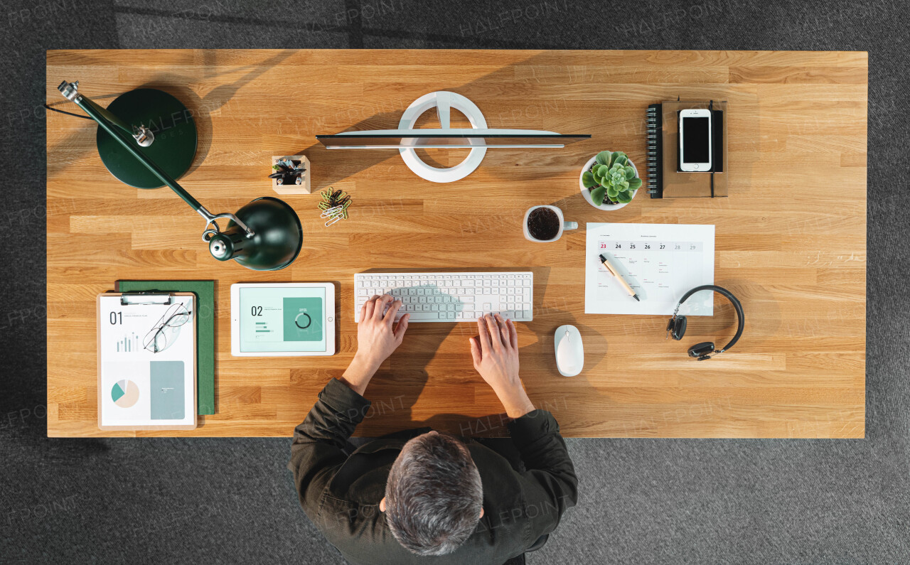 A top view of businessman working on computer at desk with paperwork in home office.